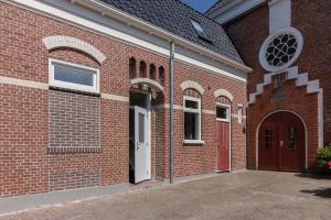 a brick building with a white door and a red doorway at Gezellig appartement in Burum