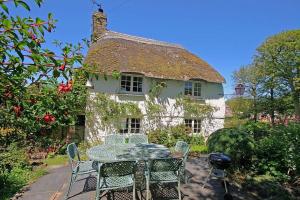 een tafel en stoelen voor een huis met rieten dak bij Putsborough Manor 3 Self Catering Cottages with Beach a short walk, dog friendly all year, On site Tennis, Play Area, Paddock, Spa baths, BBQ, Private Gardens, Superfast WIFI in Croyde