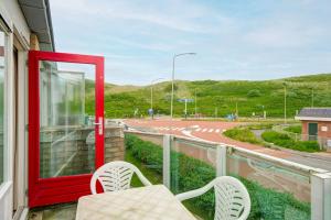 a balcony with a red door and two chairs and a road at Beach Appartement 17 - Aan de duinen, Callantsoog aan Zee in Callantsoog