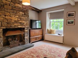 a living room with a stone fireplace and a television at Outrake Cottage in Coniston