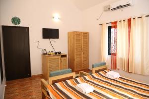 a bedroom with a bed and two chairs and a television at Villa Baywalk Goa - 200 meters from Morjim Beach in Morjim