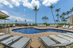a swimming pool with lounge chairs and palm trees at Island Sands 401 in Wailuku