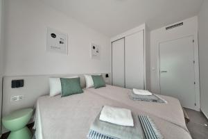 a white bedroom with a large bed with green pillows at Apartamentos Arenal 2 in Jávea +14 photos