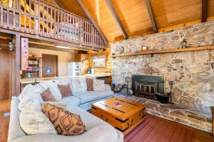 a living room with a couch and a stone fireplace at Log Cabin w Loft, Hot Tub, Deck, Fire Pit, & WiFi in Great Cacapon