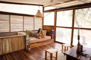 a woman sitting on a couch in a room with windows at NOSOTROS Playa Maderas - Surf House & Casitas in Playa Maderas +126 photos