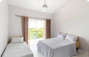 a white bedroom with two beds and a window at Triplex Belíssimo in Cabo Frio
