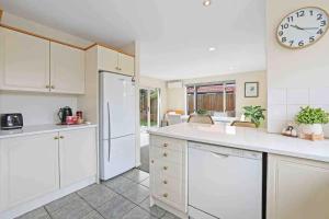 une cuisine avec des armoires blanches et une horloge au mur dans l'établissement A Great Location 4 bedrooms, quiet and comfort!, à Christchurch