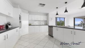 a white kitchen with white cabinets and a white tile floor at Ocean Views and Vineyards by Wine Coast Holiday Rentals in Seaford