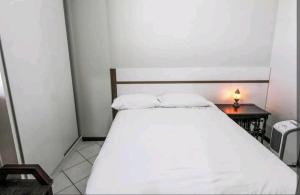 a white bed in a small room with a night stand at Flats Lago Norte MOTO CAPITAL 3 PESSOAS! in Brasilia