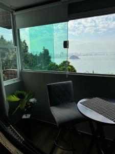 a chair and a table in a room with a large window at Apartamento Sunset House Porchat in São Vicente +8 photos