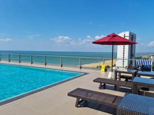 a pool with benches and an umbrella and the beach at Luxury Sea View Apartments in Negombo
