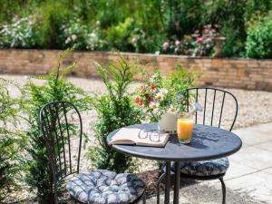 a table with a glass of orange juice and two chairs at Sweetslade Cottage in Bourton on the Water