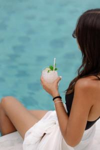 una donna seduta sulla spiaggia con in mano un drink di Pnoi Hotel a Logaras