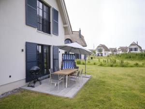 a patio with a table and chairs and an umbrella at Reetland am Meer - Premium Reetdachvilla mit 3 Schlafzimmern, Sauna und Kamin F04 in Dranske