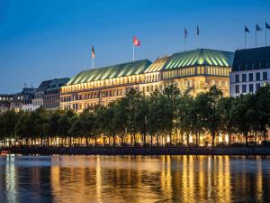 a building with flags on top of it next to a river at Fairmont Hotel Vier Jahreszeiten in Hamburg