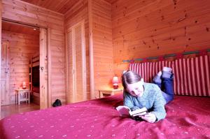 a young girl laying on a bed reading a book at Goélia - Les Chalets des Marmottes in Saint-Jean-dʼArves
