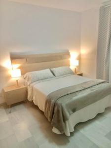 a white bedroom with a large bed with two lamps at Vivienda Cádiz in Cádiz