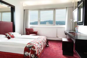 a hotel room with a bed and a desk and windows at ARCOTEL Nike Linz in Linz