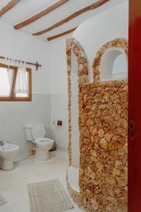 a bathroom with a toilet and a stone wall at Baobab Village in Watamu