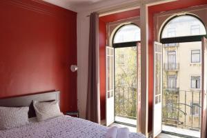 a bedroom with red walls and a bed and two windows at Nations Rooms in Lisbon