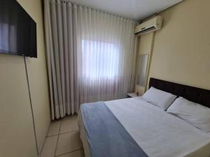 a bedroom with a white bed and a window at Kitnet 105 central com lavadora tv smart e ar condicionado in Montes Claros