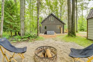 a cabin in the woods with two chairs and a fire pit at Roscommon Chalet with Hot Tub Near Higgins Lake! in Roscommon