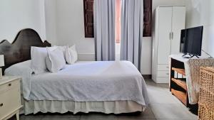 a bedroom with a bed with white sheets and a tv at Casa Kolla - 2 bedrooms with private garage in downtown Salta in Salta