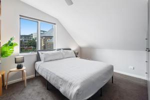 a white bedroom with a bed and a window at Convenient Bayside Living at the Edge of the City in Melbourne