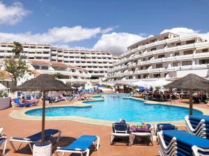 a swimming pool with chairs and umbrellas in front of a hotel at Apartamento Elisa en Garden City con piscina climatizada in Playa Fañabe