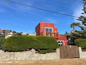 a red house with a hedge in front of it at Acogedora casa cerca del Bosque El Canelo in Algarrobo