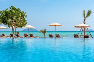 a swimming pool with chairs and umbrellas and the ocean at SAii Phi Phi Island Village in Phi Phi Islands