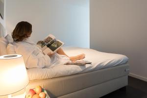 a woman sitting on a bed reading a book at Duinhotel Tien Torens in Zoutelande