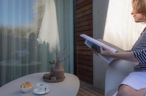 a woman sitting on a chair reading a book at Duinhotel Tien Torens in Zoutelande