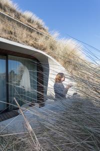 a woman sitting next to a building with a grass roof at Duinhotel Tien Torens in Zoutelande
