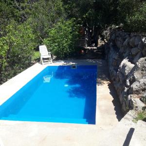 a blue swimming pool with a chair next to a stone wall at Apartment 77 with Pool and Beach in Starigrad-Paklenica