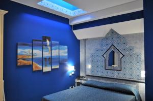 a blue bedroom with a bed and paintings on the wall at Al-Tair in San Vito lo Capo