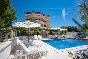 a pool with chairs and umbrellas next to a building at Pansion Villa Bok in Novalja