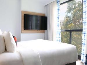 清迈Novotel Chiangmai Nimman Journeyhub的卧室里有一张白色的床和一台平板电视