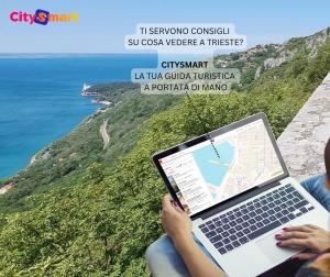 a person sitting on a cliff with a laptop at Milano Apartment in Trieste