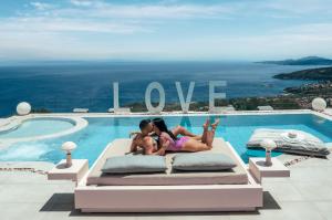 two girls laying on a bed next to a swimming pool at Emerald Villas & Suites - The Finest Hotels Of The World in Agios Nikolaos