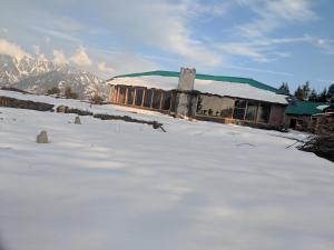 a building with snow on the ground in front of it at Wild orchid trail cottages in Jhatingr