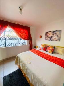 a bedroom with a bed with red curtains and a window at The Fern Corner Guest House in Nkowakowa