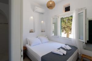 a white bedroom with a bed and a window at Aeris Tinos Suites in Panormos