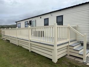a white mobile home with a deck and stairs at Visma Caravan in Llanddwywe