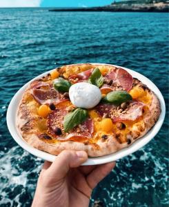 a person holding a pizza on a plate next to the water at Hotel Corallo in Santa Maria al Bagno +32 photos