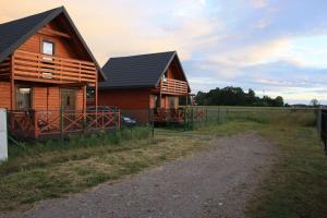 a wooden house with a fence next to a field at Domek piętrowy klimatyzowany, ogrzewany z jacuzzi na terenie ośrodka- Domki u Staszka in Rusinowo