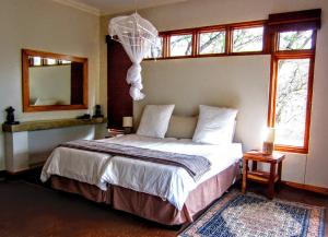 Schlafzimmer mit einem Bett, einem Spiegel und Fenstern in der Unterkunft Chumbi Bush House in Hluhluwe
