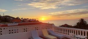 バジェエルモソにあるVv Casa Zoila A 15 Minutos del Garajonayのバルコニー(椅子2脚付)が備わり、海に沈む夕日を望めます。