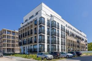 biały budynek z samochodami zaparkowanymi na parkingu w obiekcie Ambria Apartments Promenada w Świnoujściu