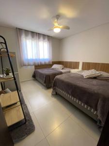 une chambre avec deux lits et un ventilateur de plafond dans l'établissement Casa 3 Condomínio Pé na Areia Ponta do Papagaio, à Palhoça
